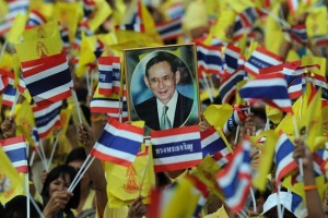 A portrait of Thai King Bhumibol Adulyadej (C) is held up by one of tens of thousands of Thais gathered outside the Anantasamakom Throne Hall as they wait for an address by King Bhumibol Adulyadej at Royal Plaza in Bangkok's historic district on December 5, 2012. Tens of thousands of Thais crowded central Bangkok on December 5 for a rare address by King Bhumibol Adulyadej, the world's longest reigning monarch, as part of celebrations for his 85th birthday.   AFP PHOTO / Christophe ARCHAMBAULT